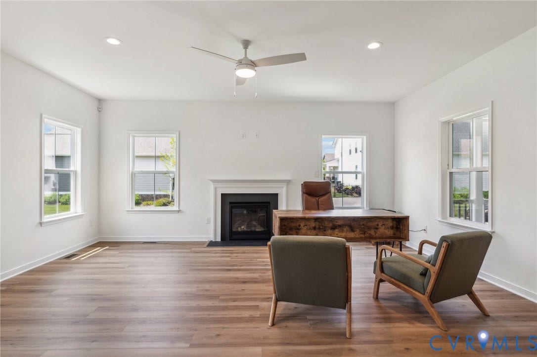 9116 TERROIR Lane, Viniterra Villas, New Kent, VA 23124 Spacious room featuring wood-finish flooring, a fireplace with a white mantel, multiple windows, recessed lighting, and a ceiling fan