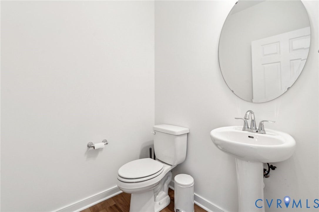 9116 TERROIR Lane, Viniterra Villas, New Kent, VA 23124 Pedestal sink with chrome-finish faucet, white toilet, oval wall mirror, and wood-finish flooring