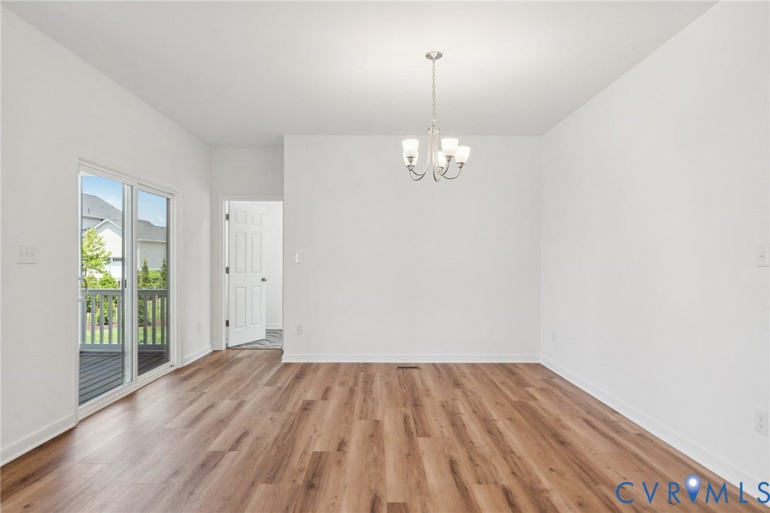 9116 TERROIR Lane, Viniterra Villas, New Kent, VA 23124 Bright, open room featuring gleaming wood-finish flooring throughout, French doors with glass panes opening to an outdoor space, white painted walls, and a polished chrome chandelier pendant fixture suspended from the ceiling