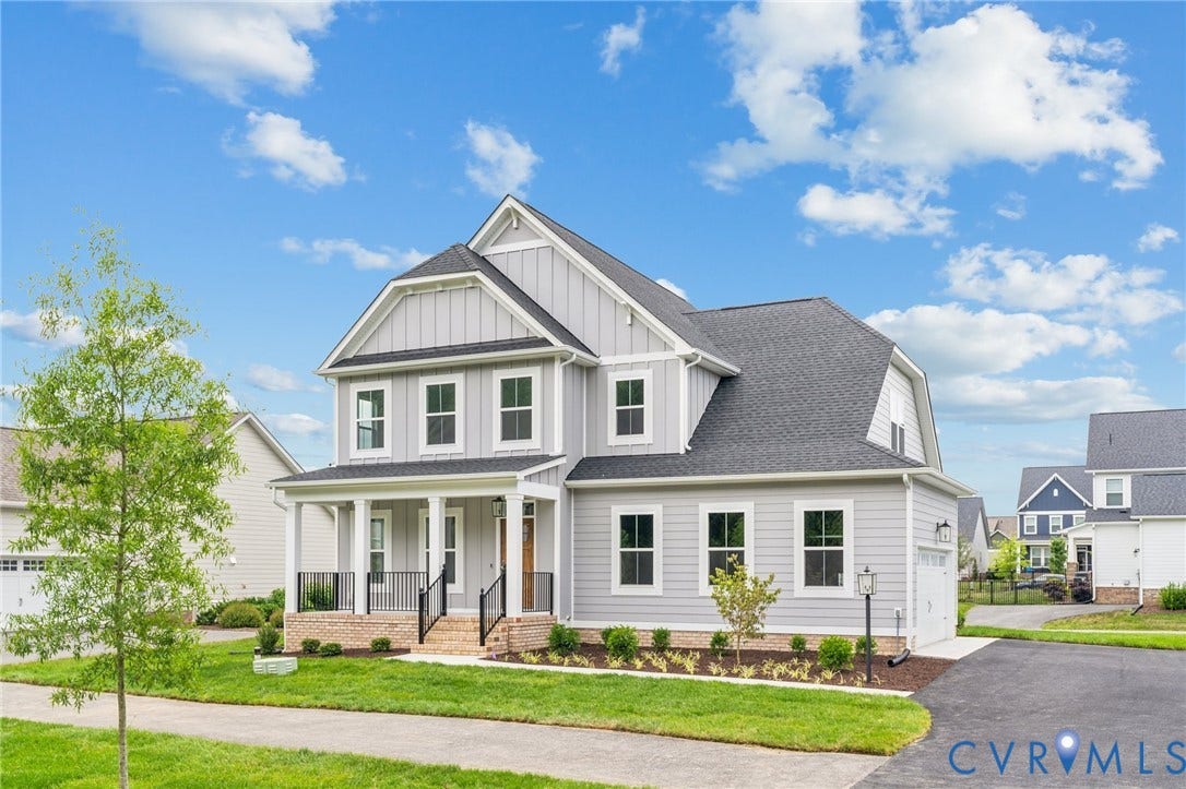9116 TERROIR Lane, Viniterra Villas, New Kent, VA 23124 Two-story residence featuring light gray siding with white trim, a covered front porch, an attached garage, a paved driveway, and manicured landscaping