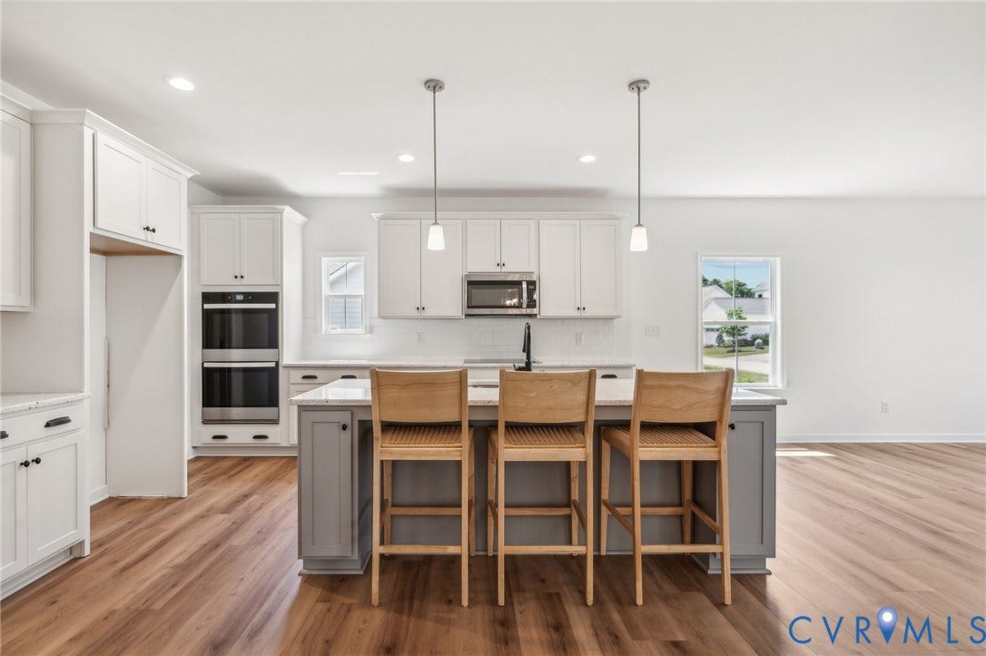 9116 TERROIR Lane, Viniterra Villas, New Kent, VA 23124 Open-concept kitchen with wood-finish flooring, white cabinetry, double wall ovens, a central island with counter seating, and pendant lighting