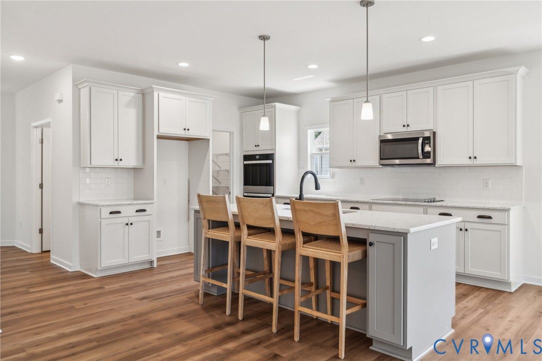 9116 TERROIR Lane, Viniterra Villas, New Kent, VA 23124 White shaker cabinetry with dark hardware, wood-finish flooring, central island with seating, stainless steel appliances, and recessed lighting