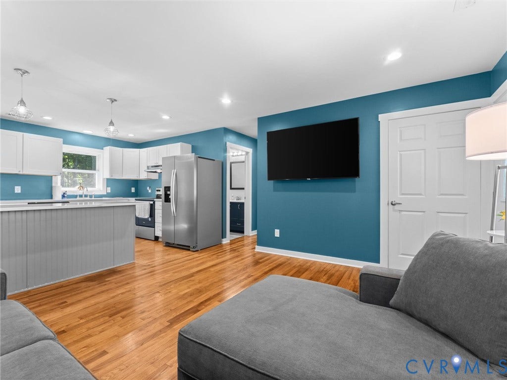 Open-concept living area with wood-finish flooring, white cabinetry, stainless steel appliances, and an island with beadboard paneling