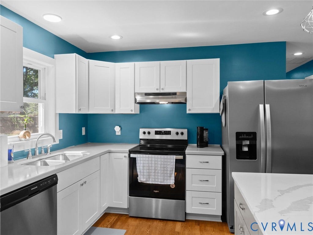 Stainless steel appliances, white shaker cabinetry, light-toned countertops, recessed lighting, and wood-finish flooring