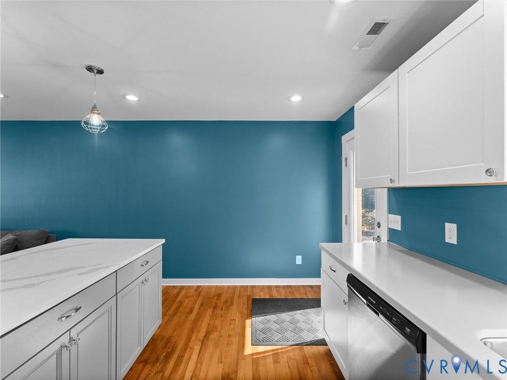 Kitchen featuring wood-finish flooring, white countertops, white upper cabinetry, and a stainless steel dishwasher