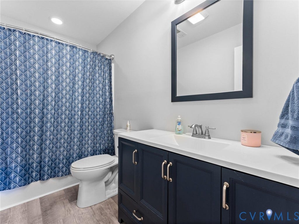 Bathroom featuring a white vanity top with an integrated sink, a dark blue vanity cabinet with silver-toned hardware, a framed mirror, and wood-finish flooring