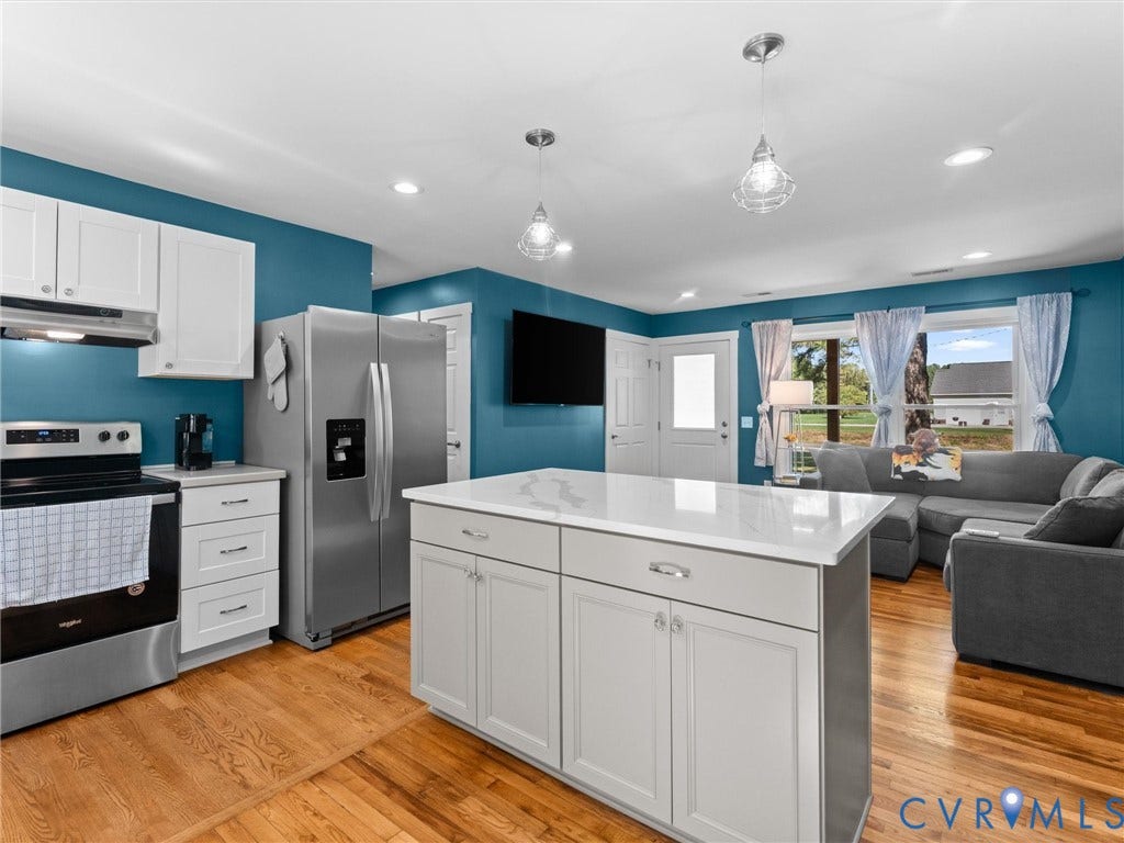 Kitchen featuring stainless steel appliances, white cabinetry, a large kitchen island with a light-toned countertop, and wood-finish flooring