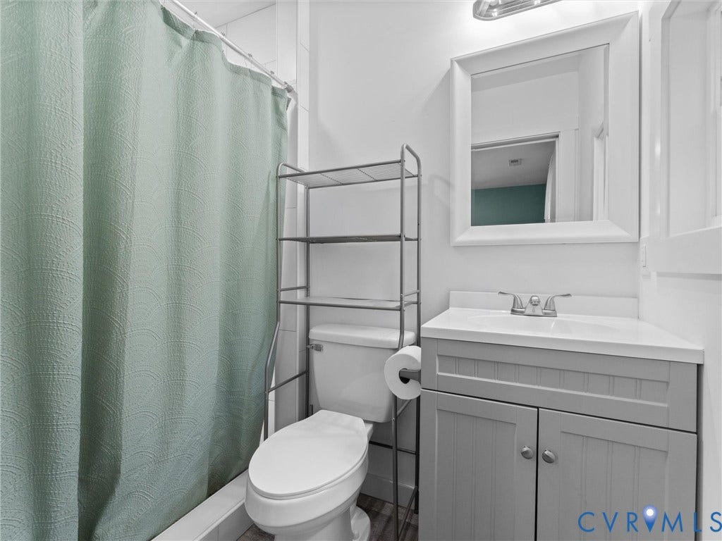 White tile shower surround, toilet, gray vanity with white countertop, chrome faucet, and framed mirror