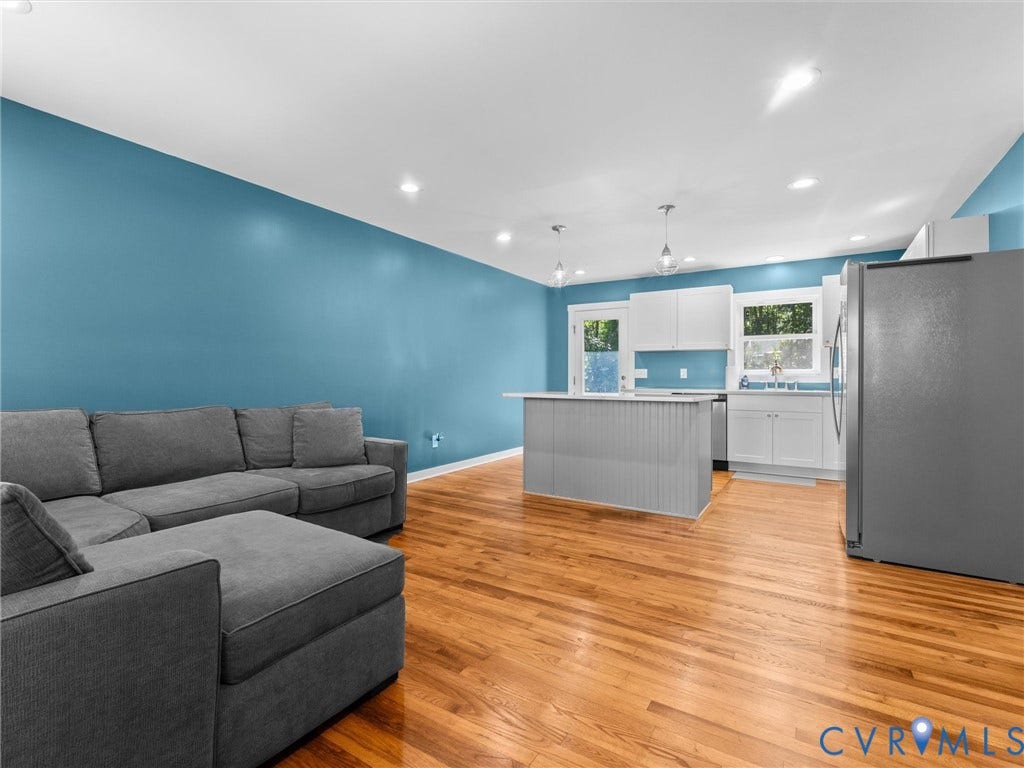 Open-concept living area featuring hardwood flooring, recessed lighting, a kitchen island with pendant lighting, white cabinetry, and stainless steel appliances