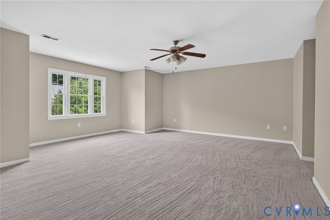 Neutral-toned walls, gray patterned carpet, ceiling fan with integrated lighting, and multiple paneled window