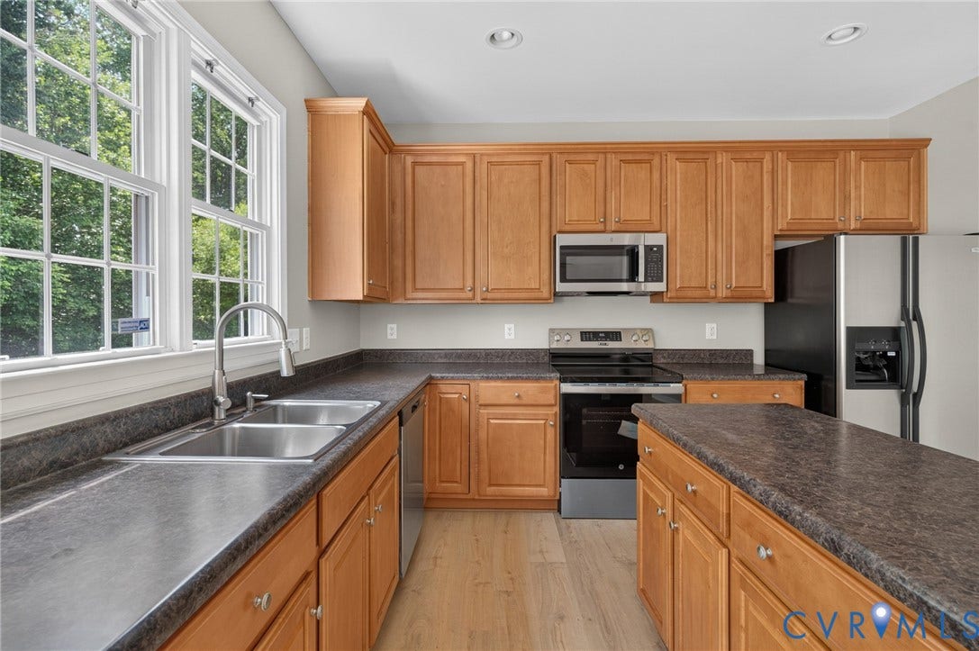 Kitchen featuring wood-finish cabinetry, dark countertops, a double basin stainless steel sink with a pull-down faucet, and stainless steel appliances