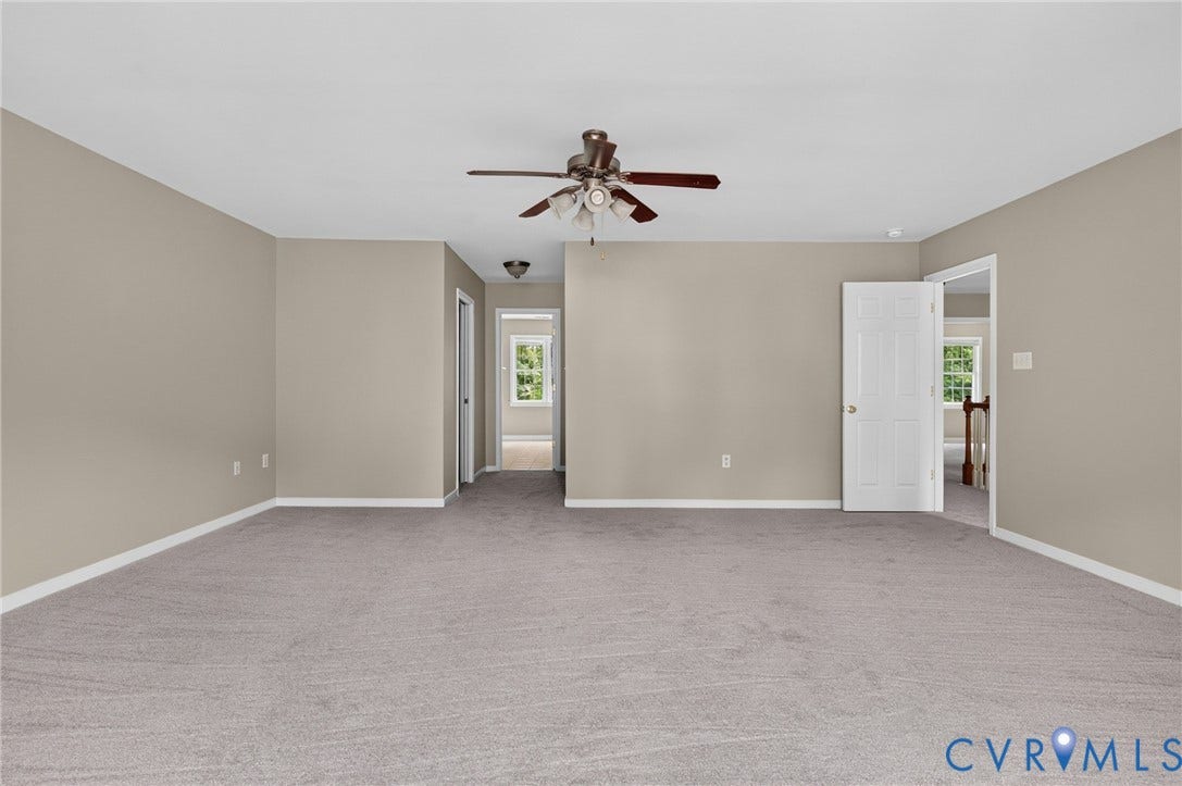 Expansive carpeted room featuring a ceiling fan, neutral wall tones, and white trim