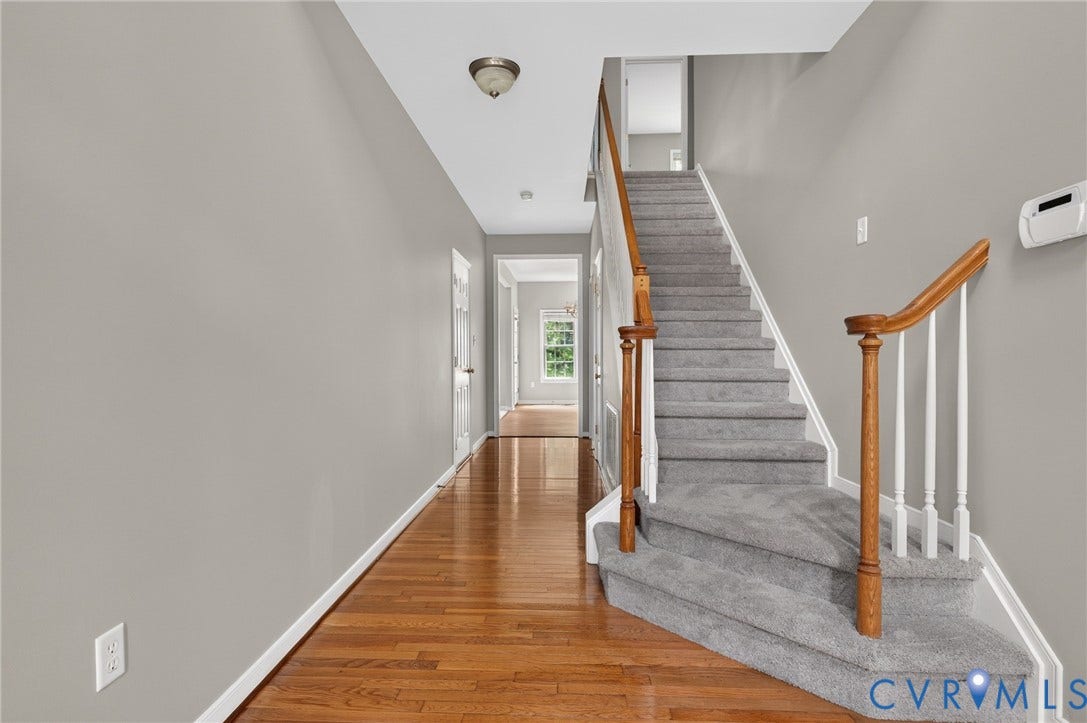 Hardwood-finish flooring, carpeted staircase, wood banister with white spindles, flush mount ceiling lighting, and light gray wall paint