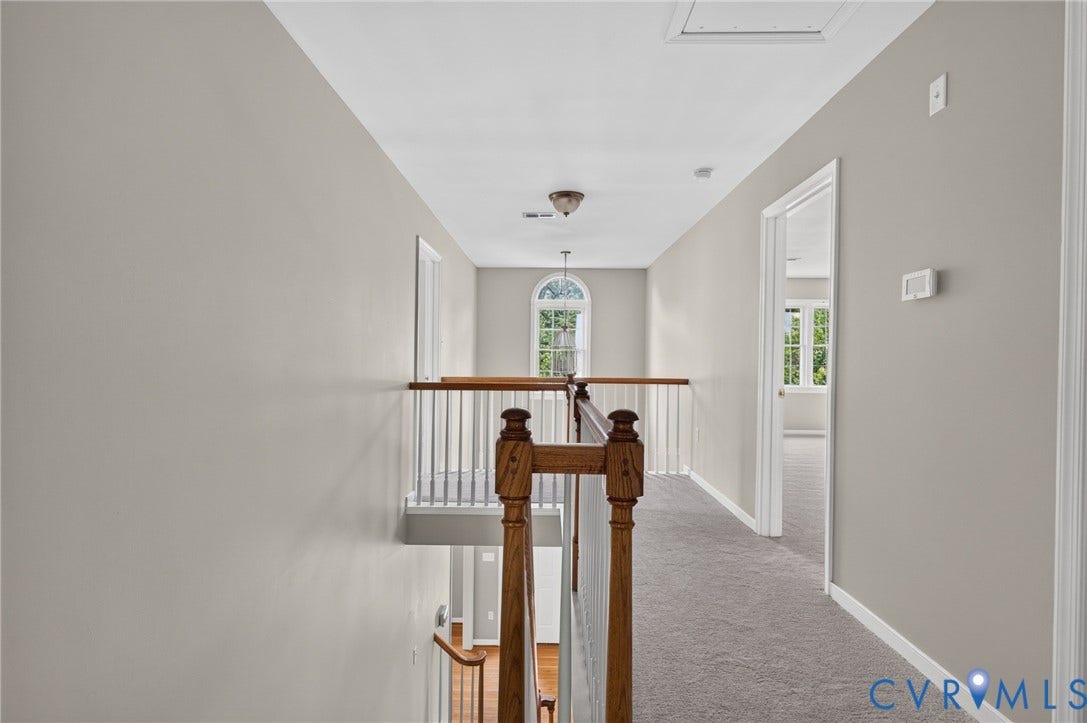 Upper-level hallway featuring a wood and white spindle railing, light gray carpeting, and an arched window
