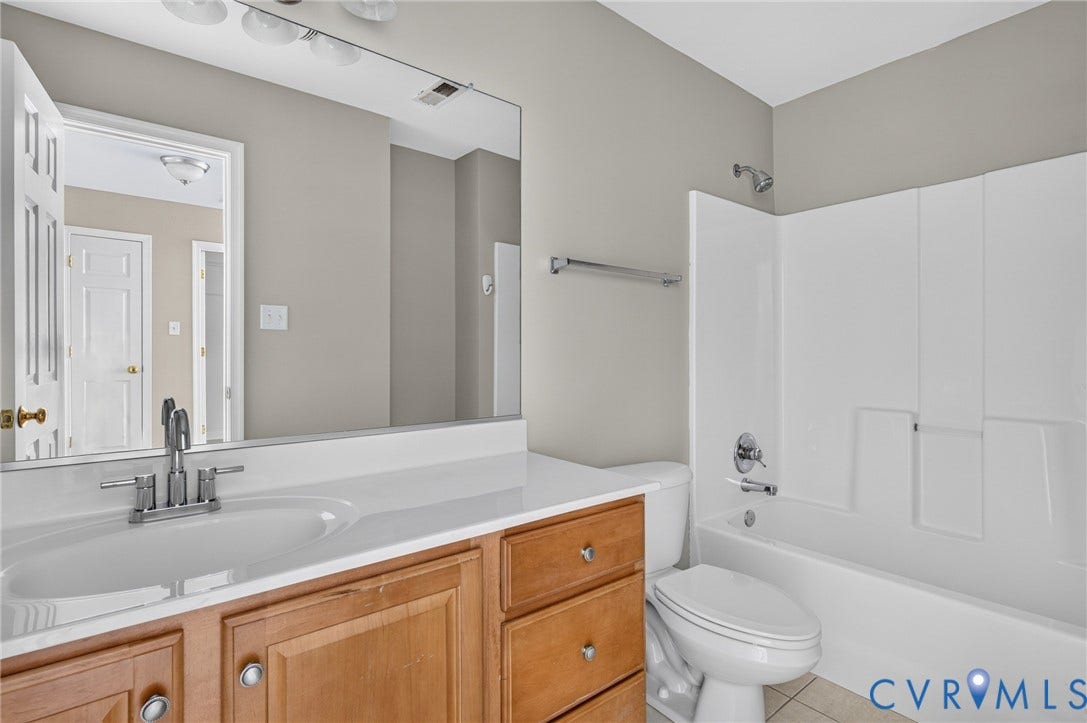 Bathroom featuring a wood-finish vanity with a white countertop and integrated sink, chrome-finish faucet, and a large wall-mounted mirror