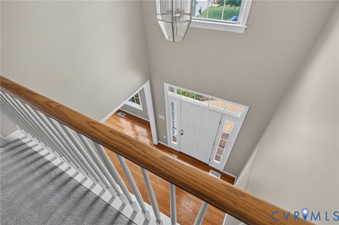 Hardwood flooring, two-story foyer, white paneled entry door with sidelights and transom window, wood banister with white spindles, and a multi-level ceiling