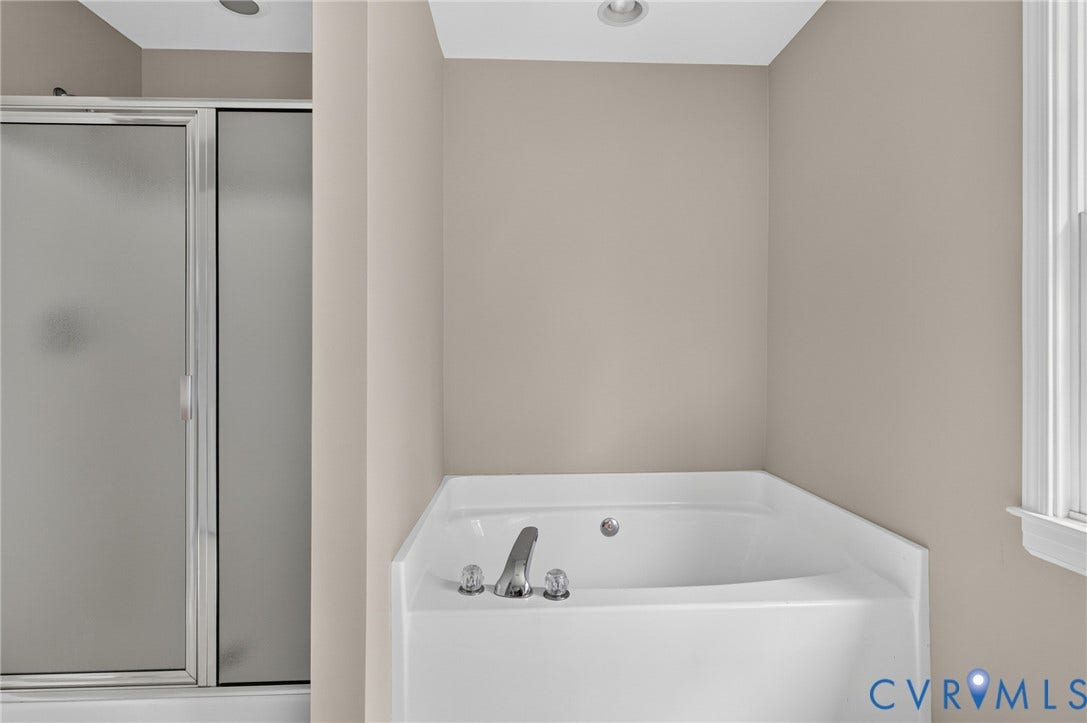 Corner soaking tub with chrome fixtures and an adjacent shower with a frosted glass enclosure