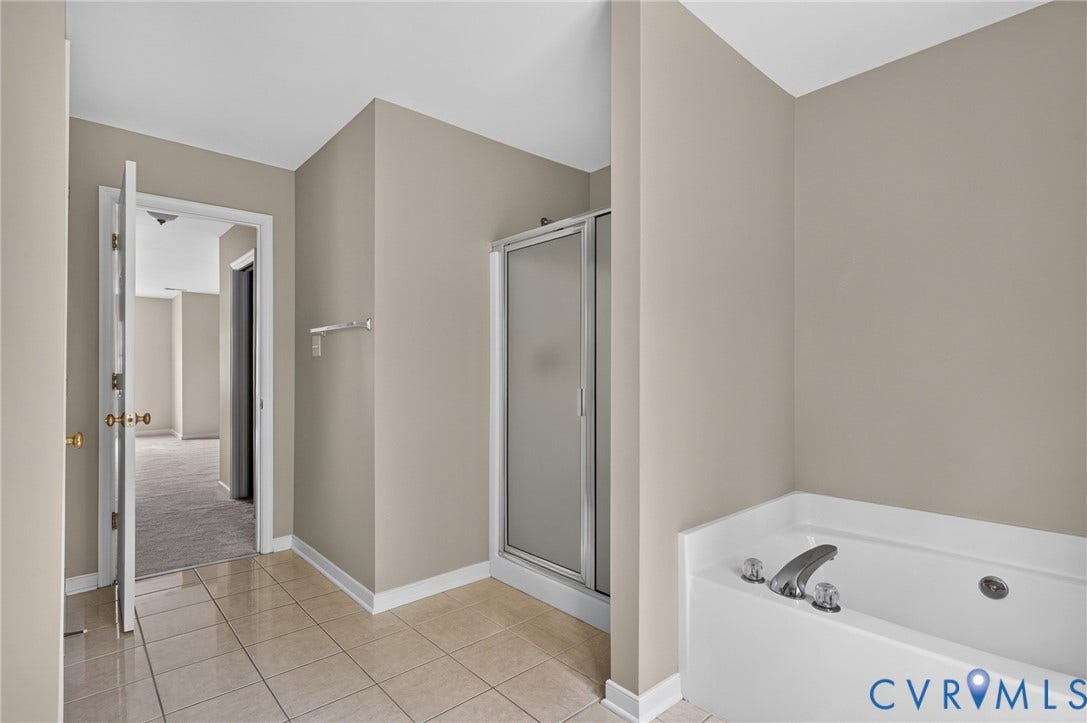 Jetted soaking tub, separate shower enclosure with frosted glass, and tile flooring
