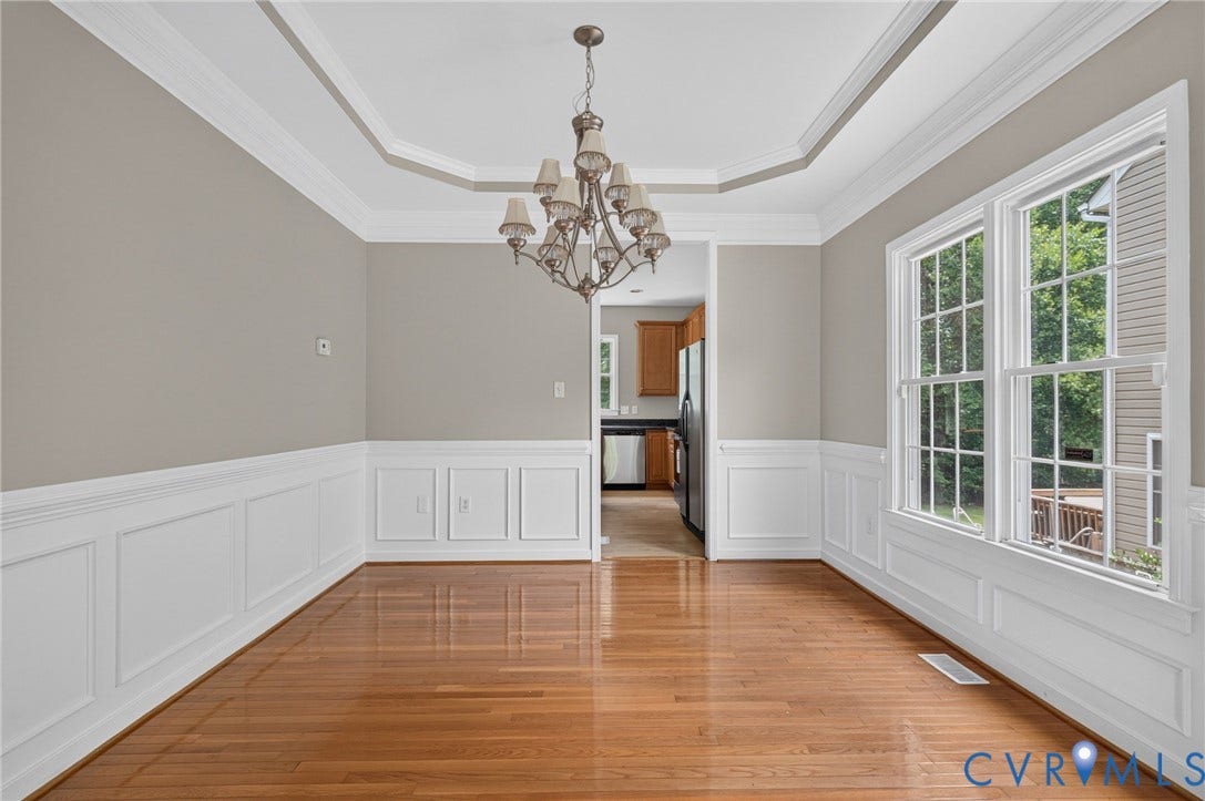 Hardwood flooring, decorative wainscoting, tray ceiling with crown molding, double-hung windows, and a chandelier