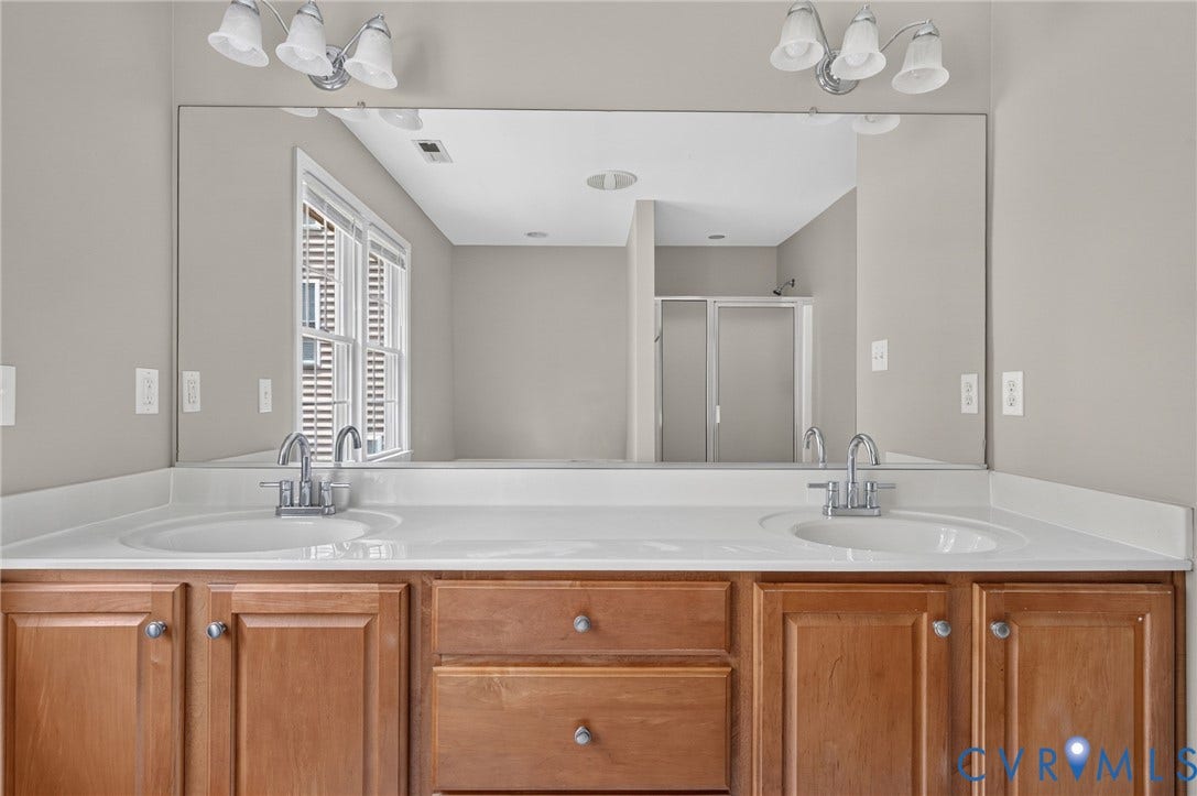 Dual vanity with light wood finish cabinetry, white solid surface countertops, and chrome fixtures