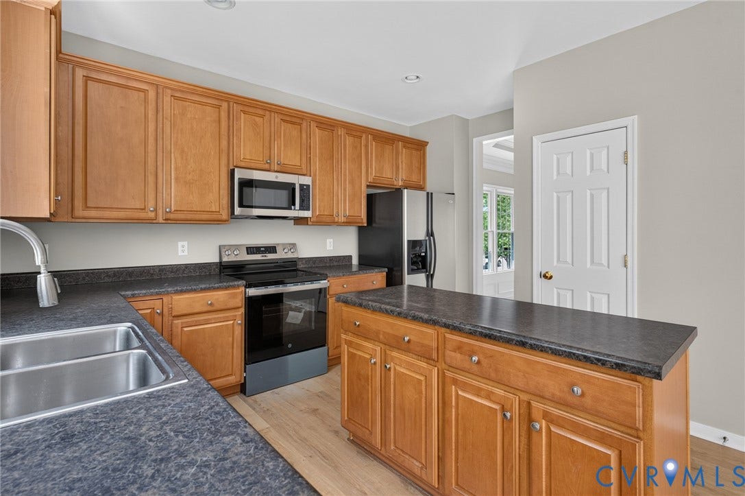 Wood-finish cabinetry with dark countertops, stainless steel appliances, and a double basin sink
