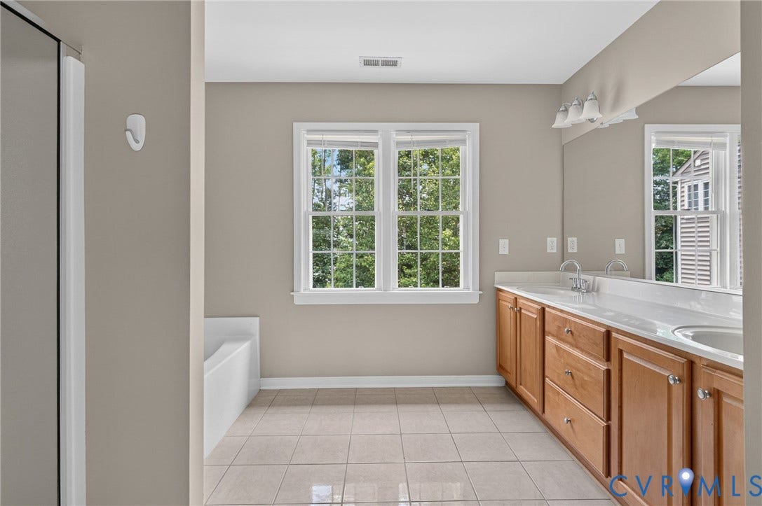Double vanity with integrated sinks, light wood-finish cabinetry, ceramic tile flooring, and a window with natural light