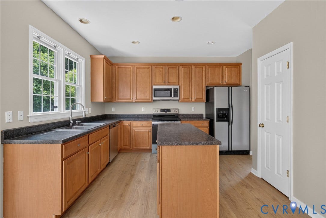 Kitchen featuring wood-finish cabinetry, dark countertops, a stainless steel double sink, and integrated stainless steel appliances