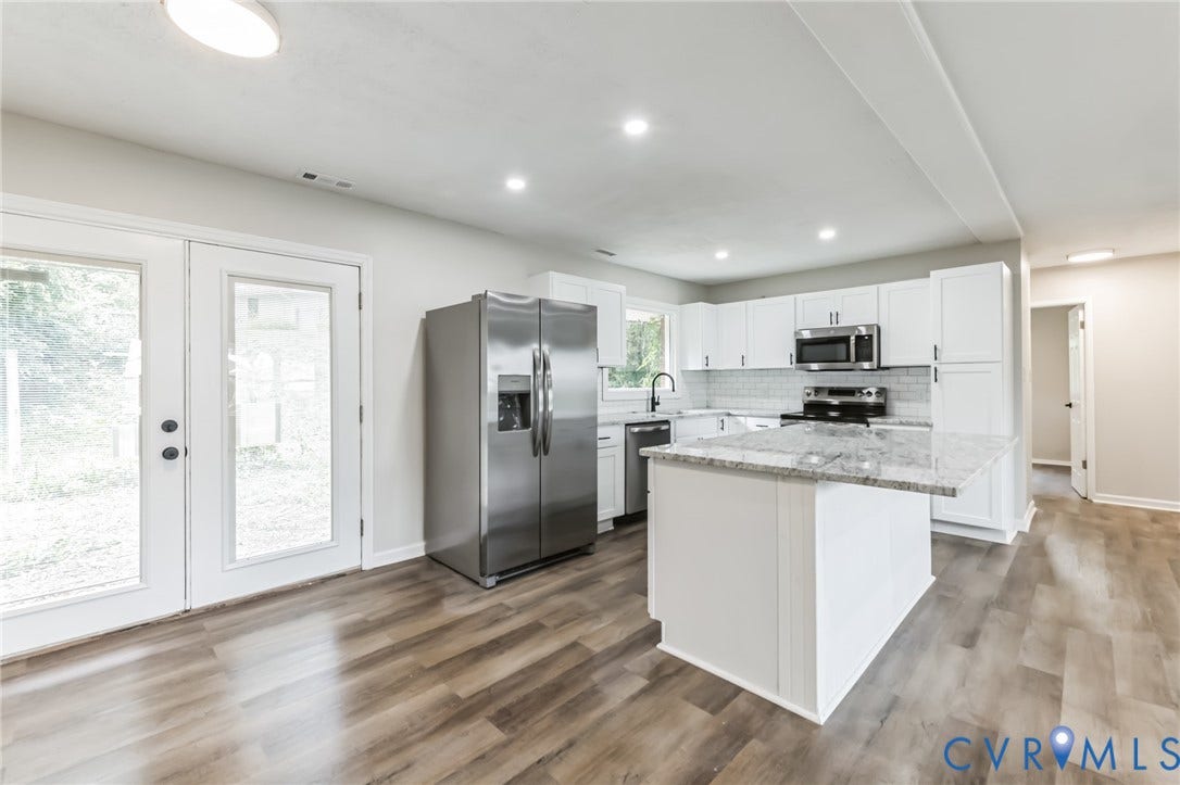 Well-appointed kitchen featuring white cabinetry, stainless steel appliances, granite countertops, and wood-finish flooring