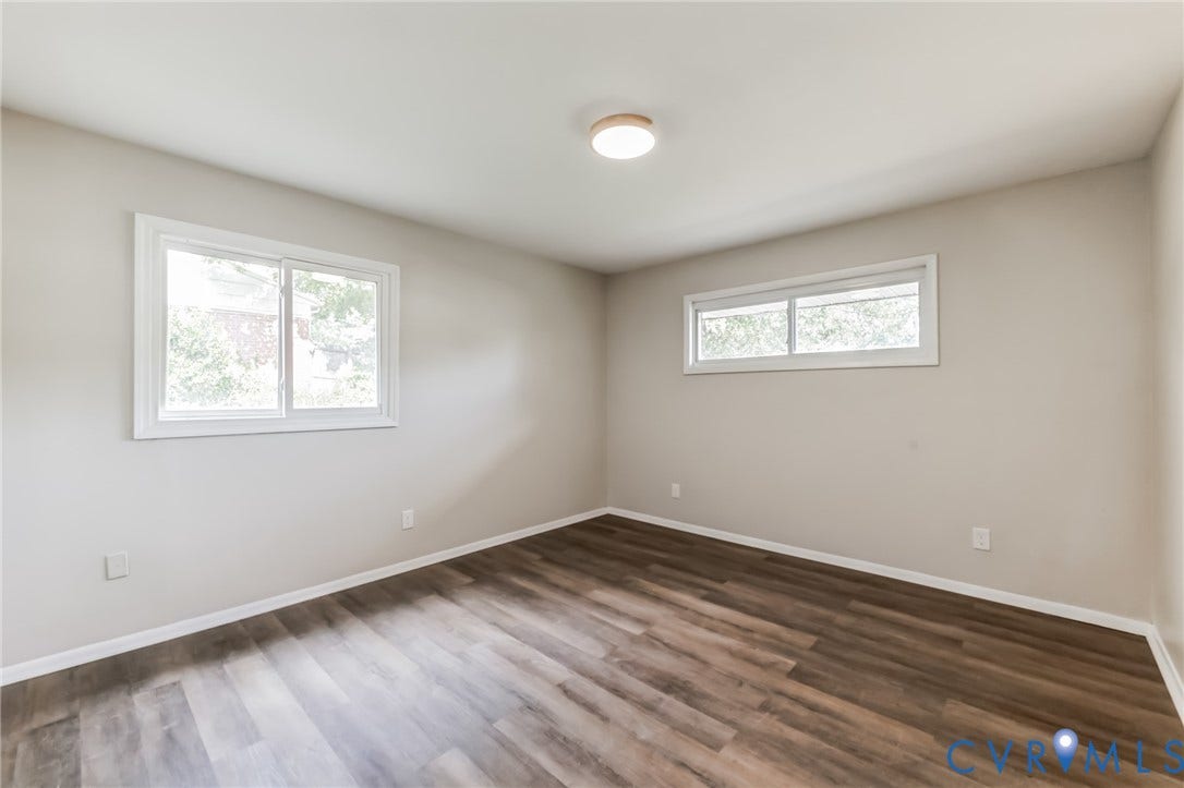 Wood-finish flooring with light neutral wall tones, two windows with white trim, and a flush-mount ceiling light
