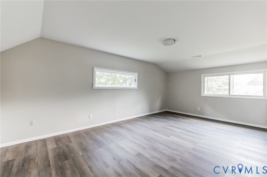 Spacious room with wood-finish flooring, light gray walls, and multiple windows