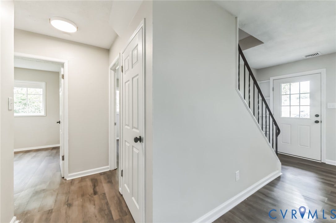 Wood-finish flooring throughout, white paneled doors with dark hardware, staircase with dark iron balusters, and a white front door with multiple glass panes