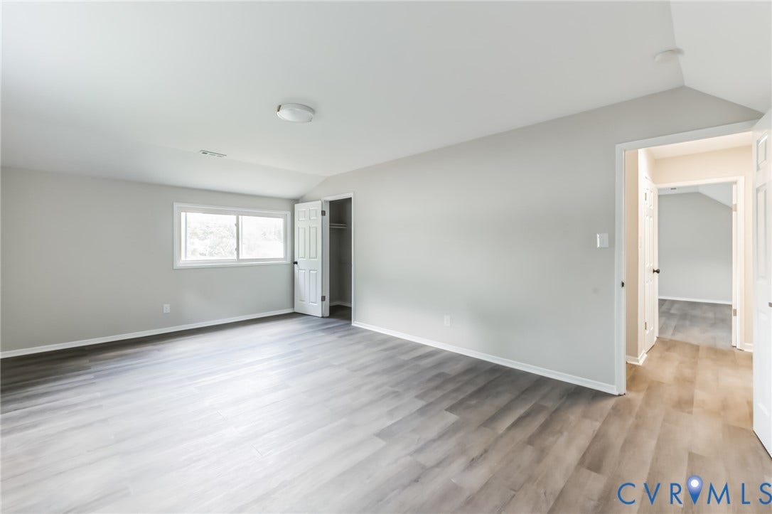 Spacious room with wood-finish flooring, light gray wall paint, and a single window with white trim