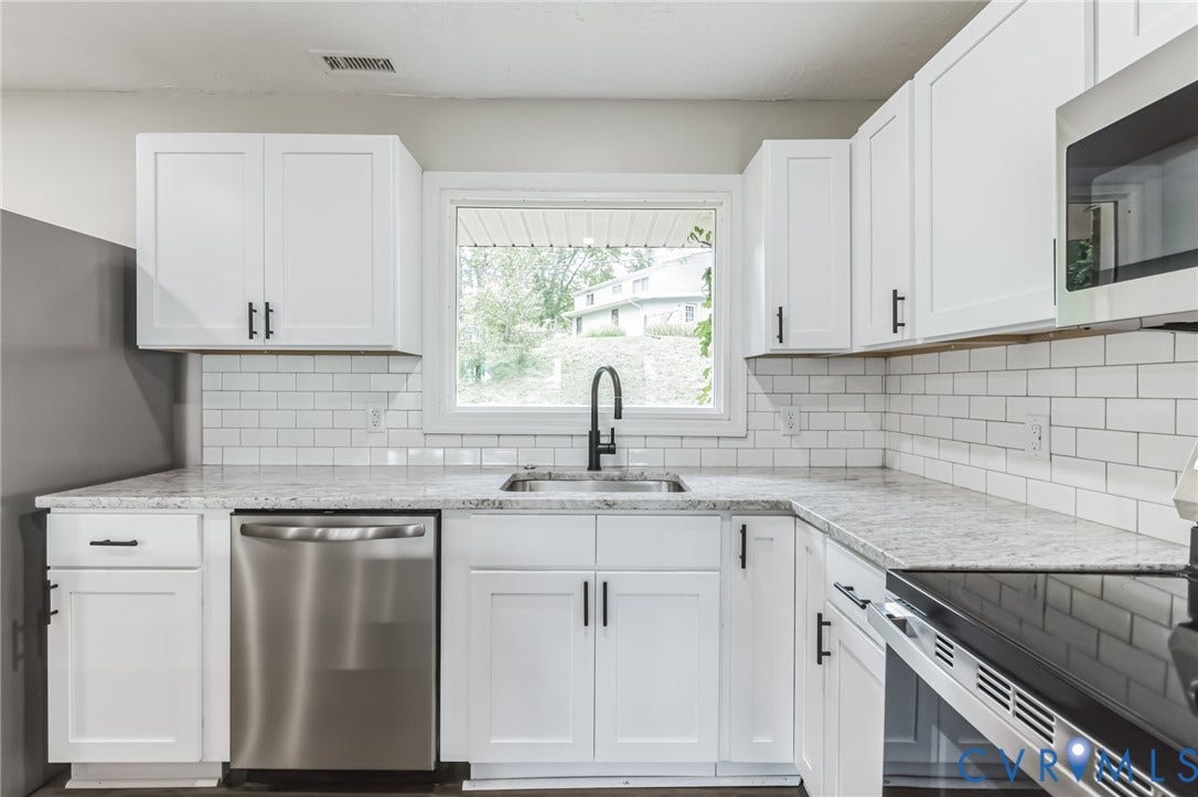 White shaker-style cabinetry with matte black hardware, stainless steel appliances, subway tile backsplash, and light-toned countertops