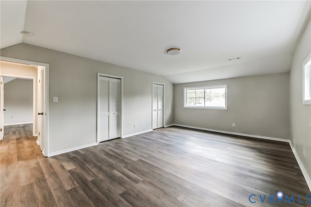 Spacious room featuring wood-finish flooring, light gray walls, white trim, and multiple windows