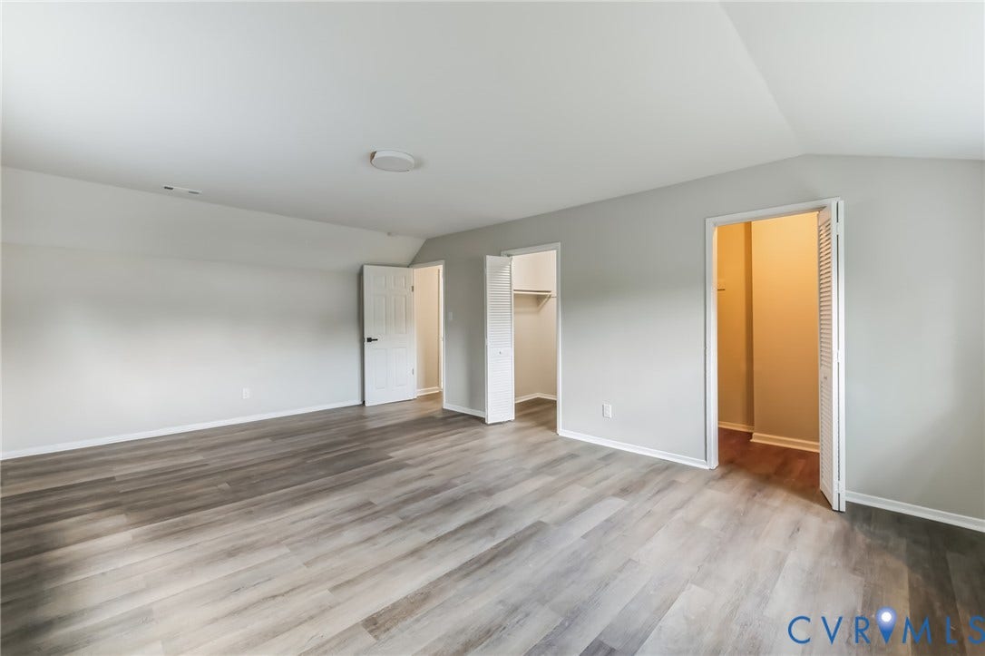 Spacious room featuring wood-finish flooring, light gray walls, white trim, and multiple doorways