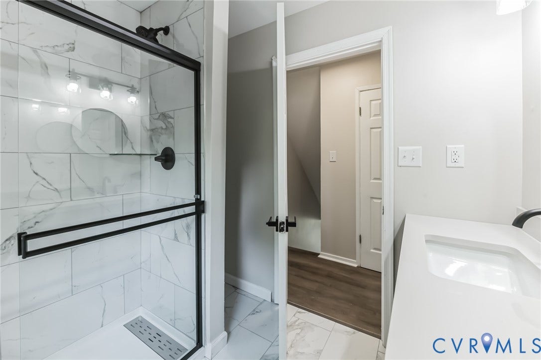 Glass-enclosed shower with matte black fixtures, white subway tile surround, integrated shower shelf, and a white shower pan