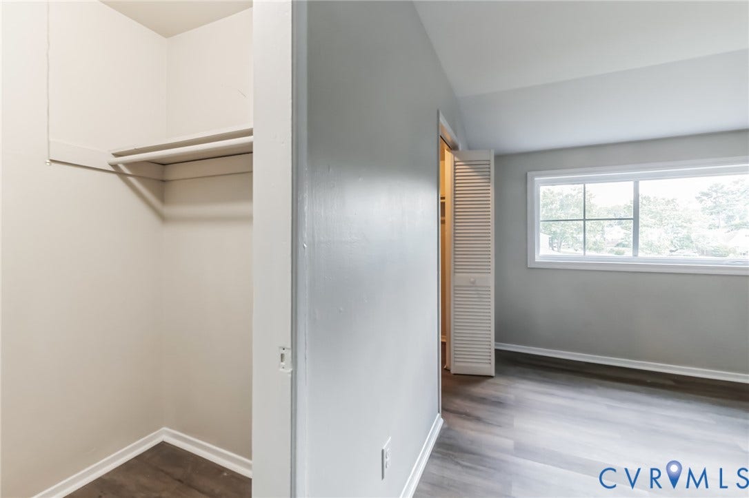 Wood-finish flooring throughout, white trim, and a window with exterior tree scenery