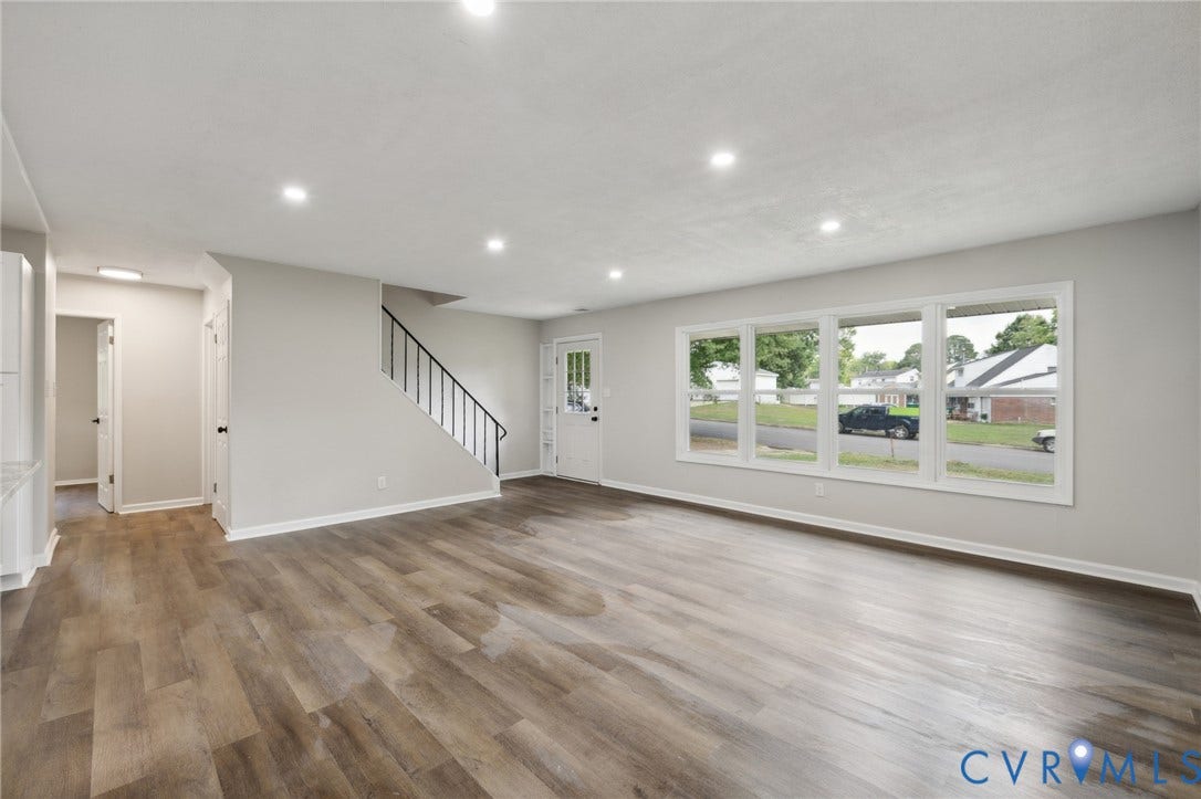 Recessed lighting, wood-finish flooring, white walls, black stair railing, and a multi-pane window
