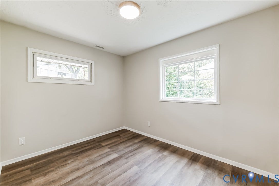 Wood-finish flooring, neutral wall color, two windows providing natural light, and a ceiling-mounted light fixture