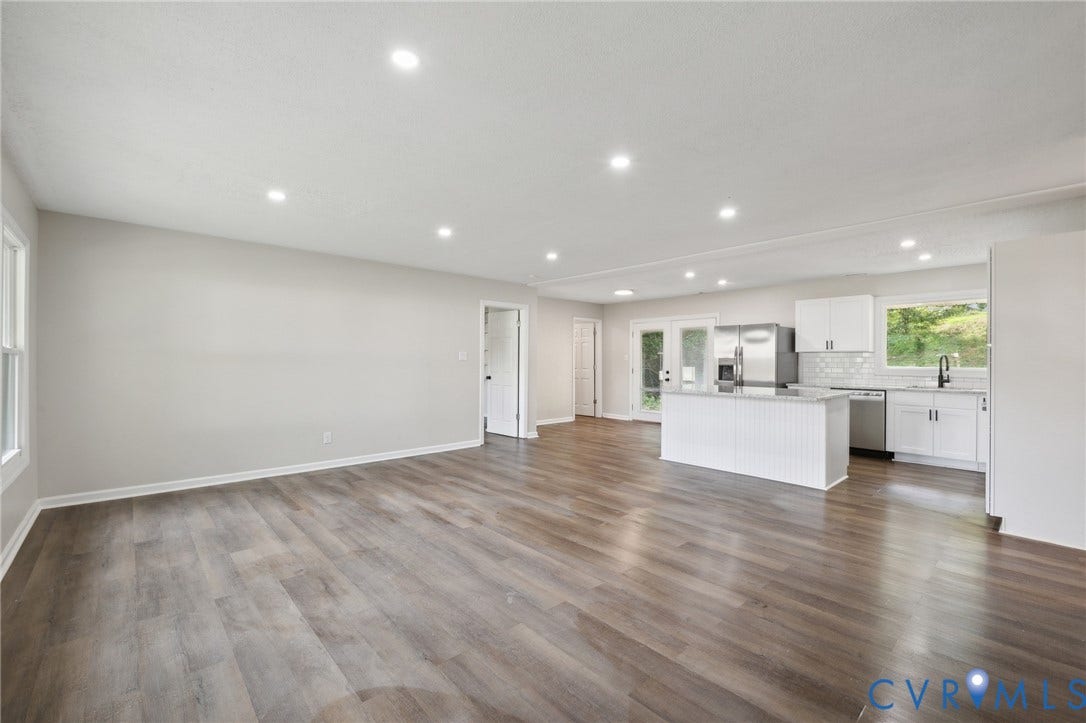Expansive living area featuring wood-finish flooring, recessed lighting, and a kitchen with white cabinetry, stainless steel appliances, and a central island