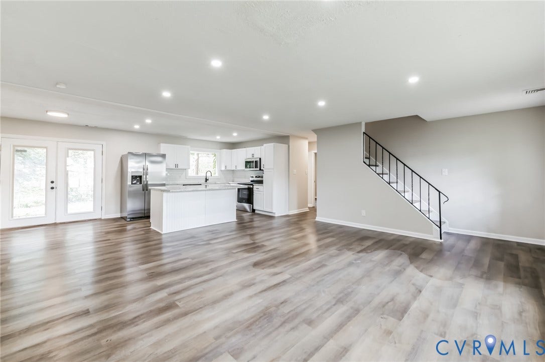 Open-concept interior featuring wood-finish flooring, recessed lighting, and a white kitchen with stainless steel appliances