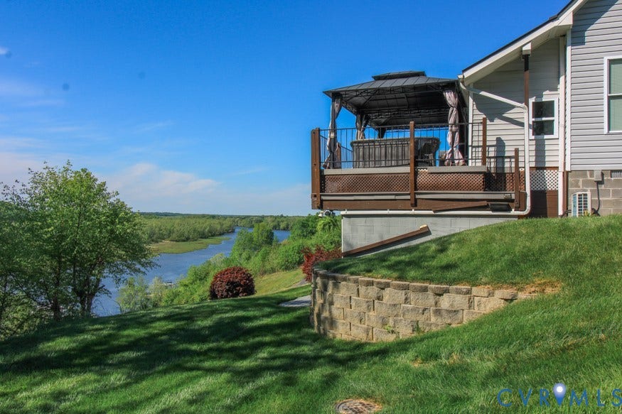 511 Riverview Court, Chester, VA 23836 Expansive elevated deck with integrated gazebo, complemented by a tiered retaining wall, manicured lawn, and natural water feature beyond