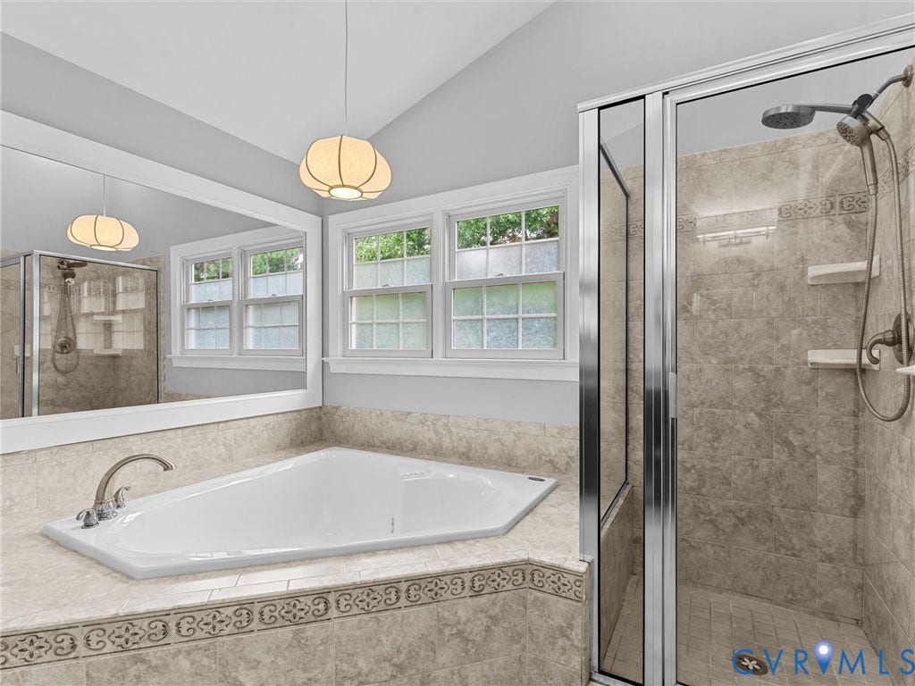 12100 English Ivy Lane, Glen Allen, VA 23059 Corner soaking tub with tile surround, glass-enclosed shower featuring stone-tile walls, double-hung windows, and pendant lighting