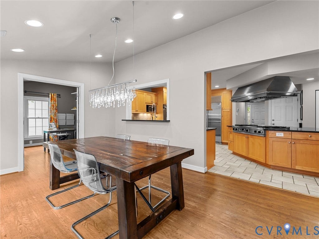 12100 English Ivy Lane, Glen Allen, VA 23059 Dining area featuring wood-finish flooring, a tiered crystal chandelier, and a pass-through window looking into the kitchen, which is equipped with custom wood cabinetry, a professional-grade stainless steel range hood, and tile flooring