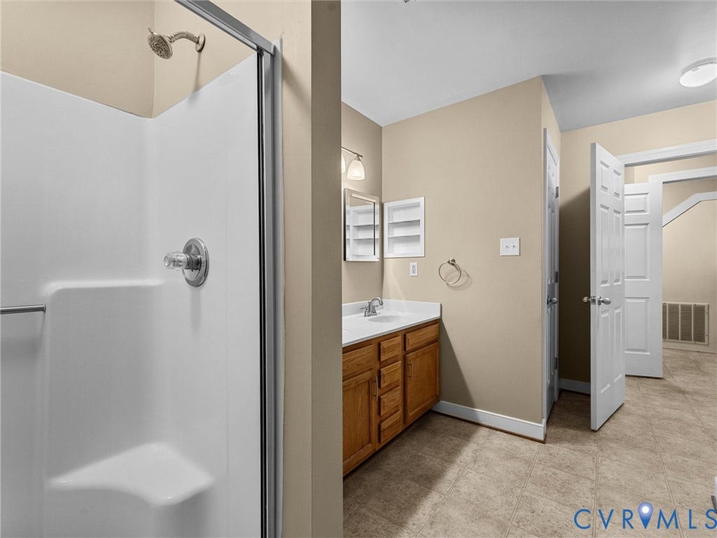 12100 English Ivy Lane, Glen Allen, VA 23059 Bathroom featuring a walk-in shower with integrated seating, wood-finish cabinetry, countertop with a single-basin sink, built-in wall shelving, and tile flooring