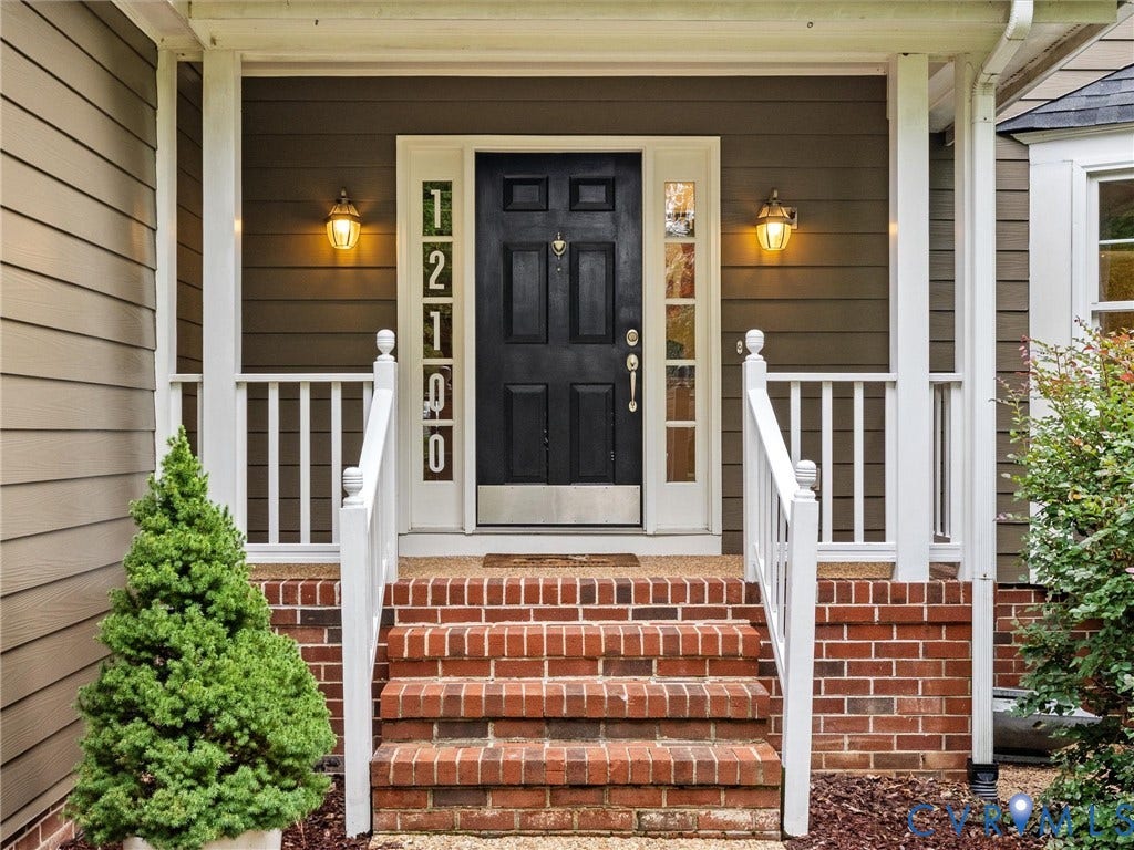 12100 English Ivy Lane, Glen Allen, VA 23059 Covered porch entry featuring a brick staircase, white wooden railings, six-panel black front door with sidelights, and exterior wall-mounted lighting