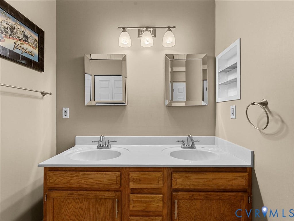 12100 English Ivy Lane, Glen Allen, VA 23059 Double vanity featuring a white countertop with dual integrated sinks, wood-finish cabinetry, two square wall-mounted mirrors, a three-light fixture, and recessed wall shelving