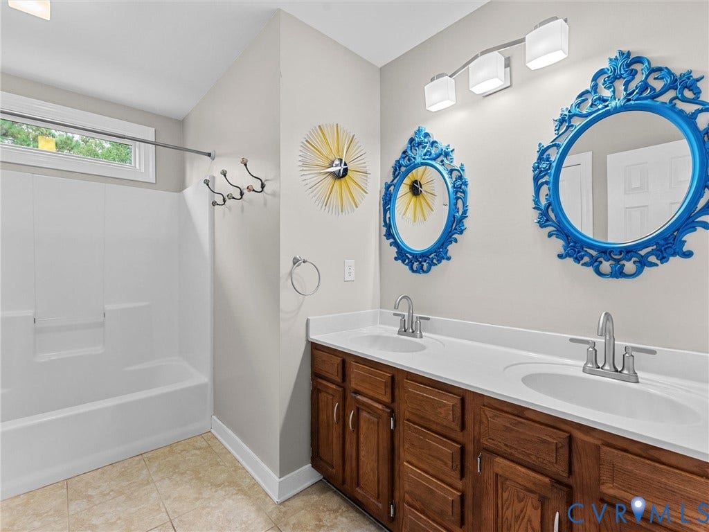 12100 English Ivy Lane, Glen Allen, VA 23059 Double vanity featuring a white countertop, two integrated sinks, brushed metal faucets, wood-finish cabinetry, and a three-light fixture above a white shower and tub surround