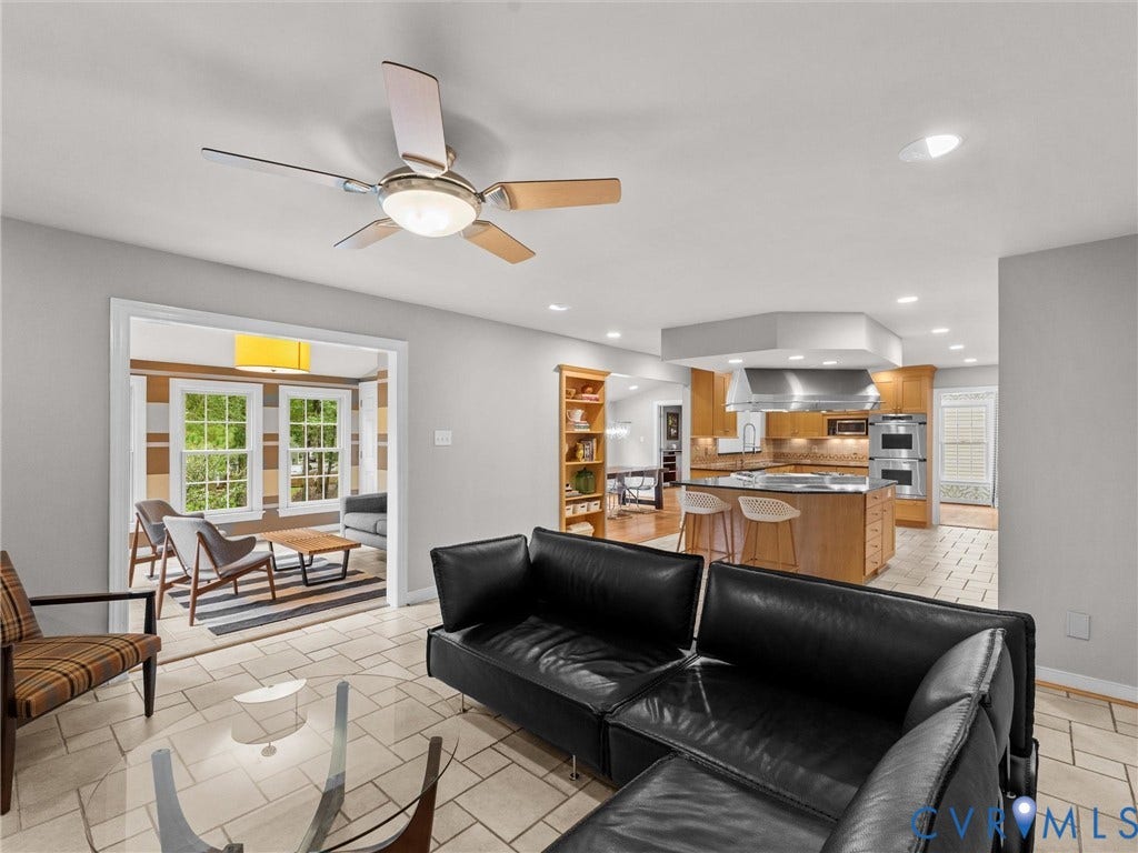 12100 English Ivy Lane, Glen Allen, VA 23059 Open-concept interior featuring light-toned tile flooring, a central kitchen island with seating, built-in wooden cabinetry, a stainless steel range hood, and a ceiling fan
