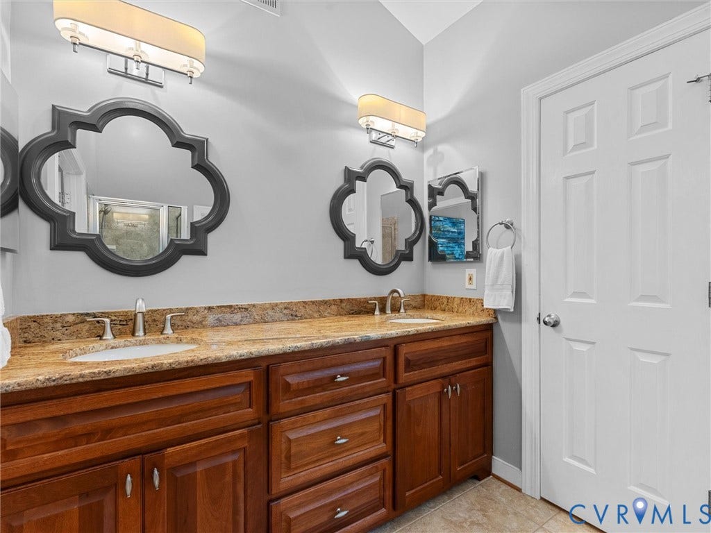 12100 English Ivy Lane, Glen Allen, VA 23059 Double vanity featuring wood cabinetry, stone-finish countertops with dual undermount sinks, decorative wall mirrors, and dual wall-mounted light fixtures